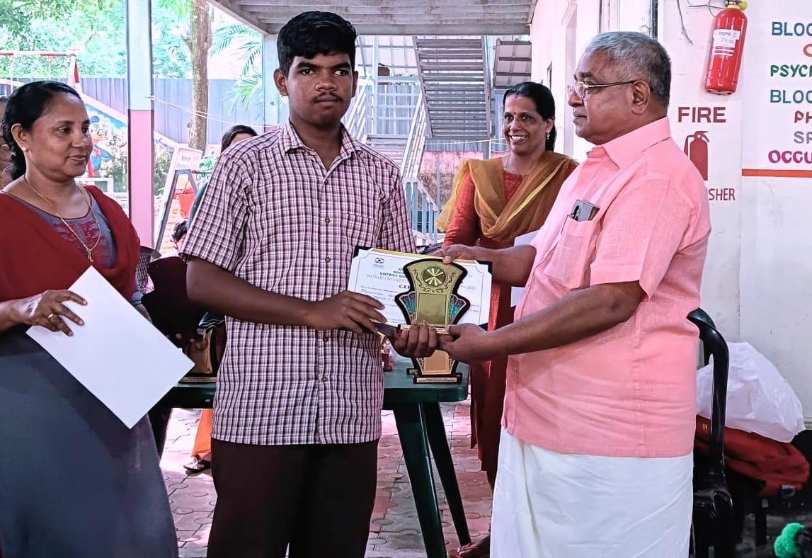 Shri D. Jacob, Chairman & Founder of Manovikas, presenting a trophy and certificate to a student in recognition of his outstanding achievement during the Kollam District-Level Competitions on the International Day of Persons with Disabilities.